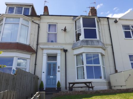 A front view of a terraced house with a blue door and bay windows at Sea Front Apartment in Hornsea
