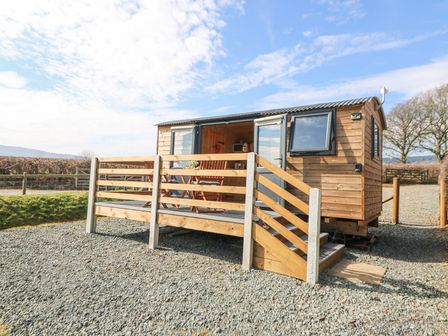 A wooden cabin with a small deck and outdoor furniture on a gravel surface at Elan in Rhayader