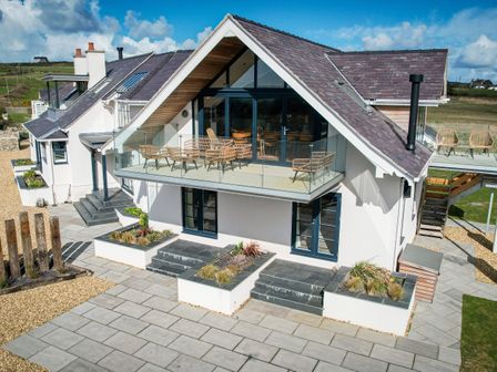 A modern house with a glass balcony and patio furniture in a rural area at Glan Towyn in Rhoscolyn