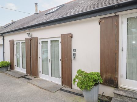 The exterior of a building with white walls brown wooden shutters and potted plants at No 1 The Hinges in Crantock