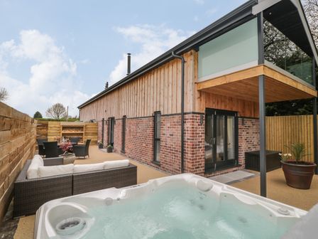 Outdoor patio area with hot tub sofa and dining table next to a brick and wood house at Lugg View in Cross Keys near Hereford