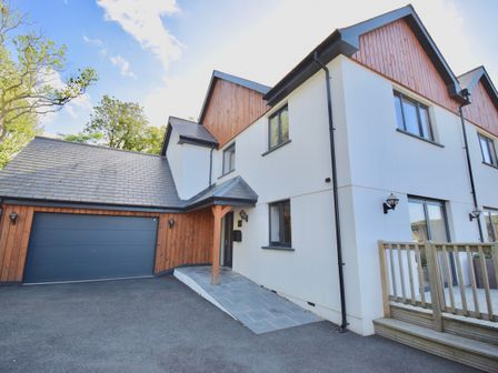 An exterior view of a two story house with wooden and white walls a driveway and a double garage door at Ty Ni in New Quay