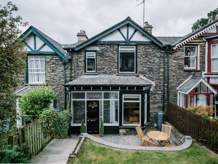 Stone exterior of a house with a black door and patio furniture in the garden at Craig Cottage in Bowness-On-Windermere