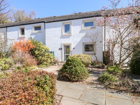 The exterior of a white cottage with a stone pathway and various shrubs at Annes Cottage in Keswick