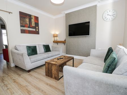A living room with two sofas green cushions a wooden coffee table a wall-mounted tv and a clock at Apartment 1 - Llandudno Central in Llandudno