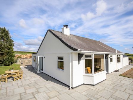 A white bungalow with a slate roof and patio area with a small wooden picnic table at Mynydd Mwyn in Penmynydd near Llanfairpwllgwyngyll