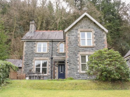 A stone house with windows a blue door outdoor table and chairs and trees in the background at Ty Capel in Betws Y Coed