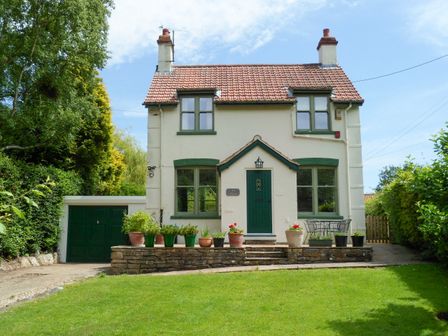 A detached house with a red tile roof green window frames and door with potted plants on a stone ledge and a green lawn at Applegarth in Cloughton