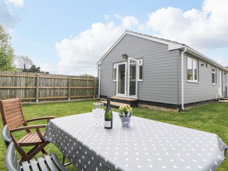 A garden with a table covered by a grey star patterned cloth and chairs outside a grey house at The Lodge in Dawlish Warren
