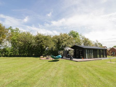 A large grass lawn with a black modern building and outdoor seating area at The Tractor Shed in Lower Broadheath Worcester