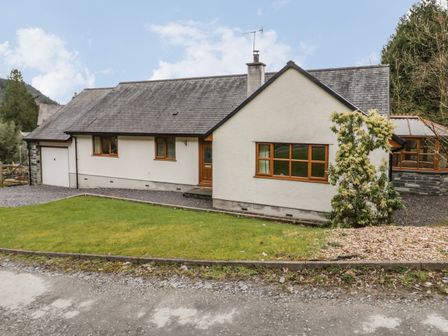 A single-story house with white walls and a slate roof with a grassy front yard and a small tree at Bryn Elsi in Betws-Y-Coed