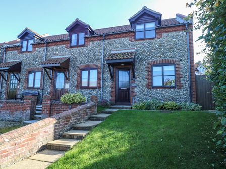 Front exterior of a row of pebble stone cottages with gardens and stairs at Seaview Cottage in Salthouse Norfolk