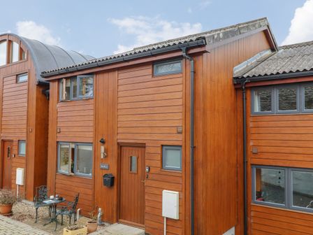 The exterior of a wooden house with windows, a door, and outdoor a table with two chairs at Maple in Falmouth