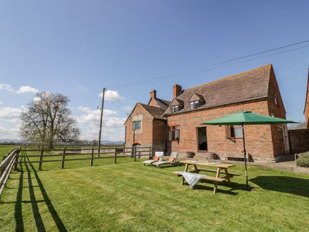 A brick house with a fenced grassy yard and outdoor seating with umbrella at Manor Farm Cottage in Hill Croome near Upton Upon Severn