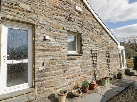 Exterior stone wall of a house with a white door and window and several potted plants at The Old Smithy Cottage Maentwrog near Penrhyndeudraeth