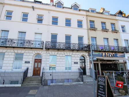 Exterior of a row of white buildings with balconies and doors including a restaurant named ENZO at Bliss On The Bay Weymouth