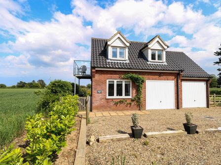 A brick house with two white garage doors and a balcony overlooking a field at Spinney's Den in Knapton