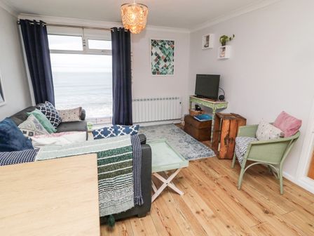 A living room with a sofa by a window overlooking the sea a TV on a table and a green chair at Sea Snug in Spittal