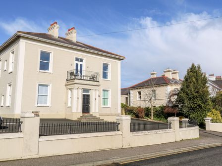 A two-story house with a balcony and black front door behind a low wall with metal fencing at Sea Breeze in Ballycastle