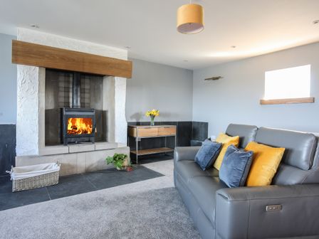 A living room with a fireplace a grey sofa with pillows and a wooden side table with flowers at The Elberry in Newborough