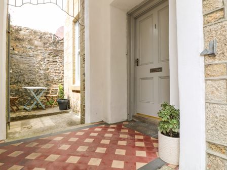 An outdoor entrance area with a closed door numbered 1 a potted plant on the floor and a small courtyard with a table and two chairs at 1 Regents Mews in Penzance