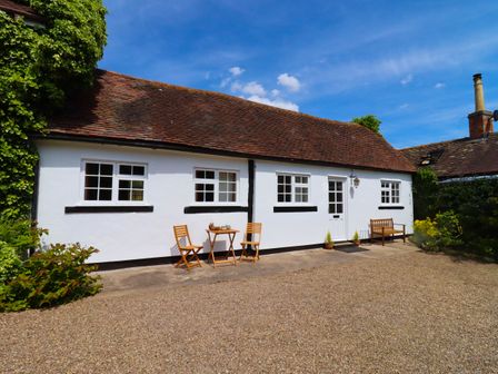 A white cottage with a tiled roof a small wooden table and chairs and a bench outside Mortons Cottage Castlemorton near Malvern