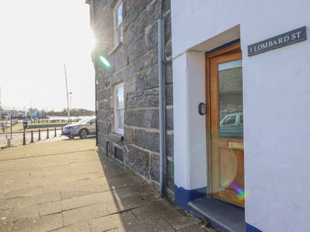 A stone and white wall building with a wooden door and a sign reading 1 Lombard St near a parked car and marina at Harbourside in Porthmadog