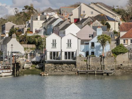 A waterfront with houses on a hillside and boats docked at the shore at Oak Cottage in Hooe