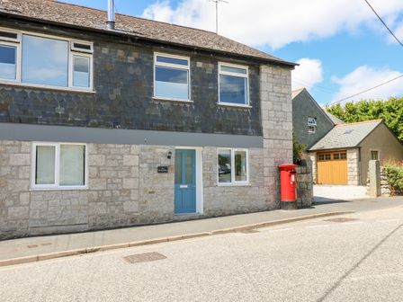 A stone and slate house with a blue door and a red post box on the sidewalk in front of the house