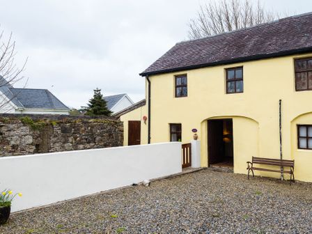 An exterior courtyard with a bench and gravel ground outside a yellow building at The Stable in Fethard-On-Sea County Wexford