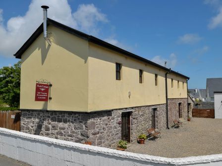 A stone and yellow two-story building with benches and potted plants outside at The Barn in Fethard-On-Sea County Wexford