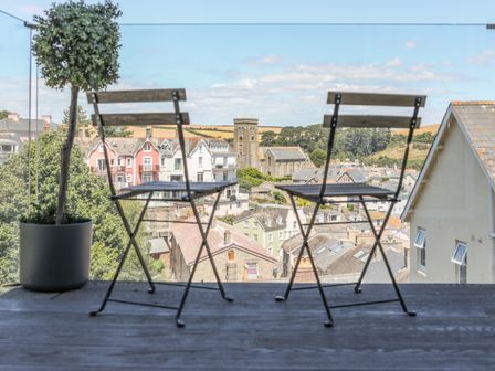 Two wooden chairs on a balcony with a glass railing overlooking houses and a church in a town