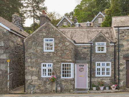 A stone house with white framed windows and a pink door with flowers at The Toll House in Dolgellau