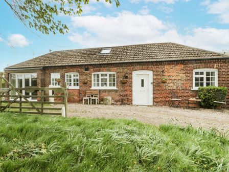 A brick house with white windows and door surrounded by grass and a wooden gate at Chestnut Cottage in Filey