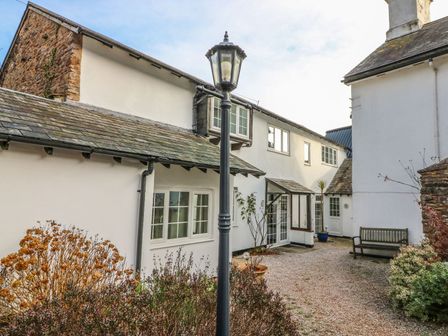 An exterior courtyard area with white buildings wooden bench and lamppost at Rose Cottage in Marldon