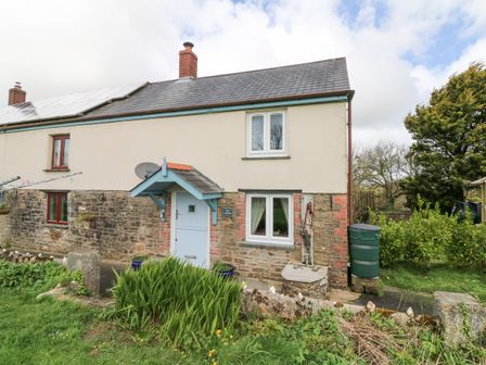 A stone and plaster cottage with a blue door and small garden at The Linhay in Holsworthy