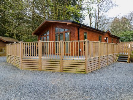 A wooden cabin with a large deck and railing surrounded by trees at Oakwood Lodge Langdale 3 White Cross Bay Windermere