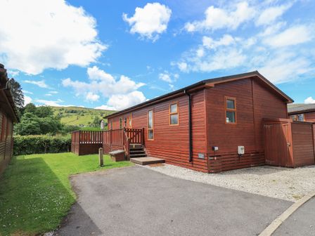 A wooden cabin with a small deck and steps leading to the entrance surrounded by grass and a paved driveway at Wansfell Retreat Lodge Wansfell 4 Limefitt Park near Windermere