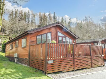 A wooden lodge with a fenced deck surrounded by grass and trees at Limefitt Lodge Fellside 8 Limefitt Park near Windermere