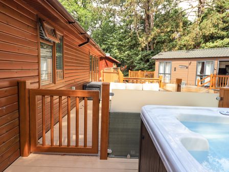 An outdoor deck with a hot tub wooden gate wooden fence and wooden cabins surrounded by trees at Lakes Lodge Keswick Court 3 White Cross Bay near Windermere