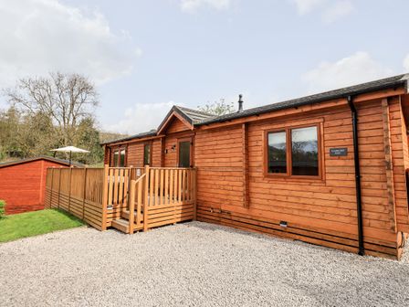 A wooden cabin with a fenced porch and gravel driveway at Ramblers Rest Lodge Pinewood 22 Limefitt Park near Windermere