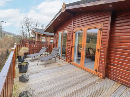 An outdoor wooden deck with two lounge chairs and potted plants outside a wooden cabin with glass doors at Horseshoe Lodge Wansfell 5 Limefitt Park near Windermere