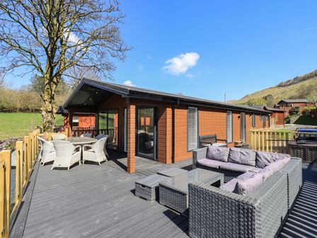 An outdoor deck area with wicker seating and dining table attached to a wooden lodge in a rural setting Jinnyspinner Lodge in Beckside 37 Limefitt Park near Windermere