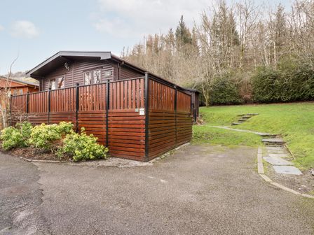 A wooden lodge with a large fenced deck and surrounding greenery at Rowan Lodge Pinewood 16 Limefitt Park near Windermere