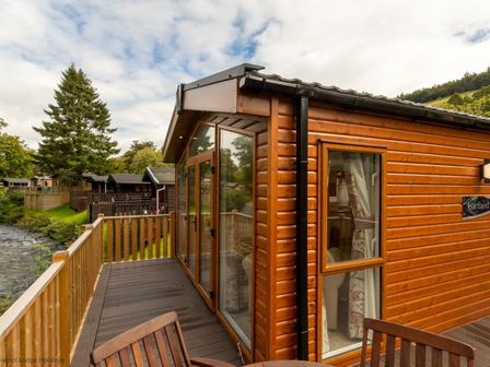 A wooden balcony with chairs outside a cabin near a river at Latterbarrow Lodge in Beckside 46 Limefitt Park near Windermere