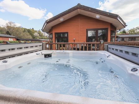 A hot tub on a deck outside a wooden cabin at Sunny Brow Lodge Lakeside 5 White Cross Bay near Windermere