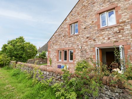 Stone house with open doors and windows surrounded by low stone wall and greenery at Rainbow Cottage in Bolton near Appleby-In-Westmorland