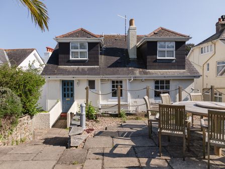 A house with two dormer windows and a blue door next to an outdoor patio with a round table and wooden chairs at Seascape in Salcombe