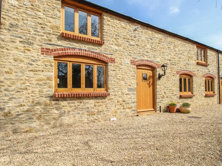An exterior view of a stone house with wooden windows and door on a gravel ground at The Stables Burton Bradstock