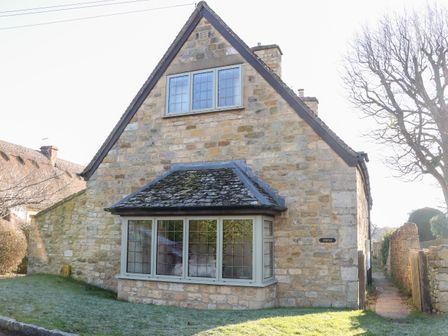 A stone house with leaded glass windows and a small front lawn at Cowfair Cottage in Chipping Campden
